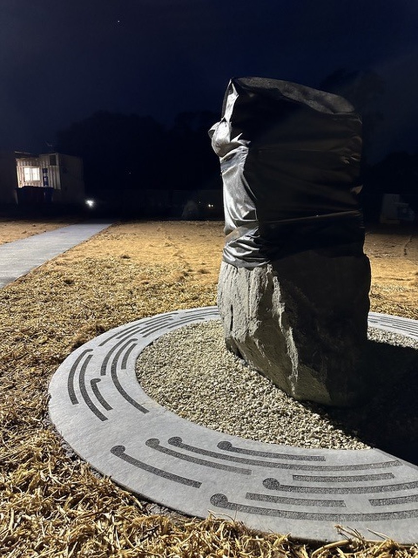 A tall standing stone wrapped for installation on a circular metal disc, photographed at night