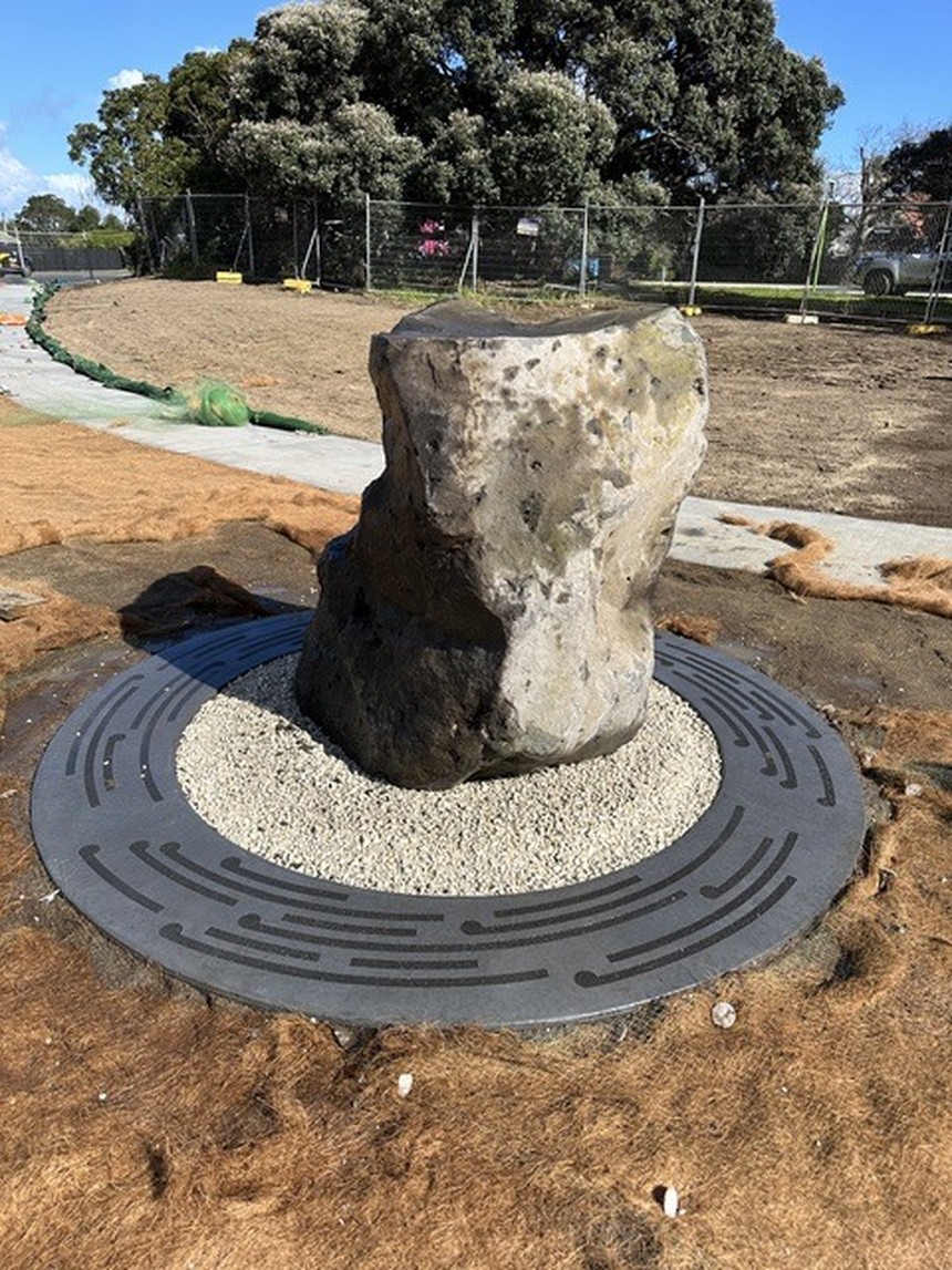 Stone Through Line: a rough quarried stone set upright on a circular perforated-metal disc bedded in gravel