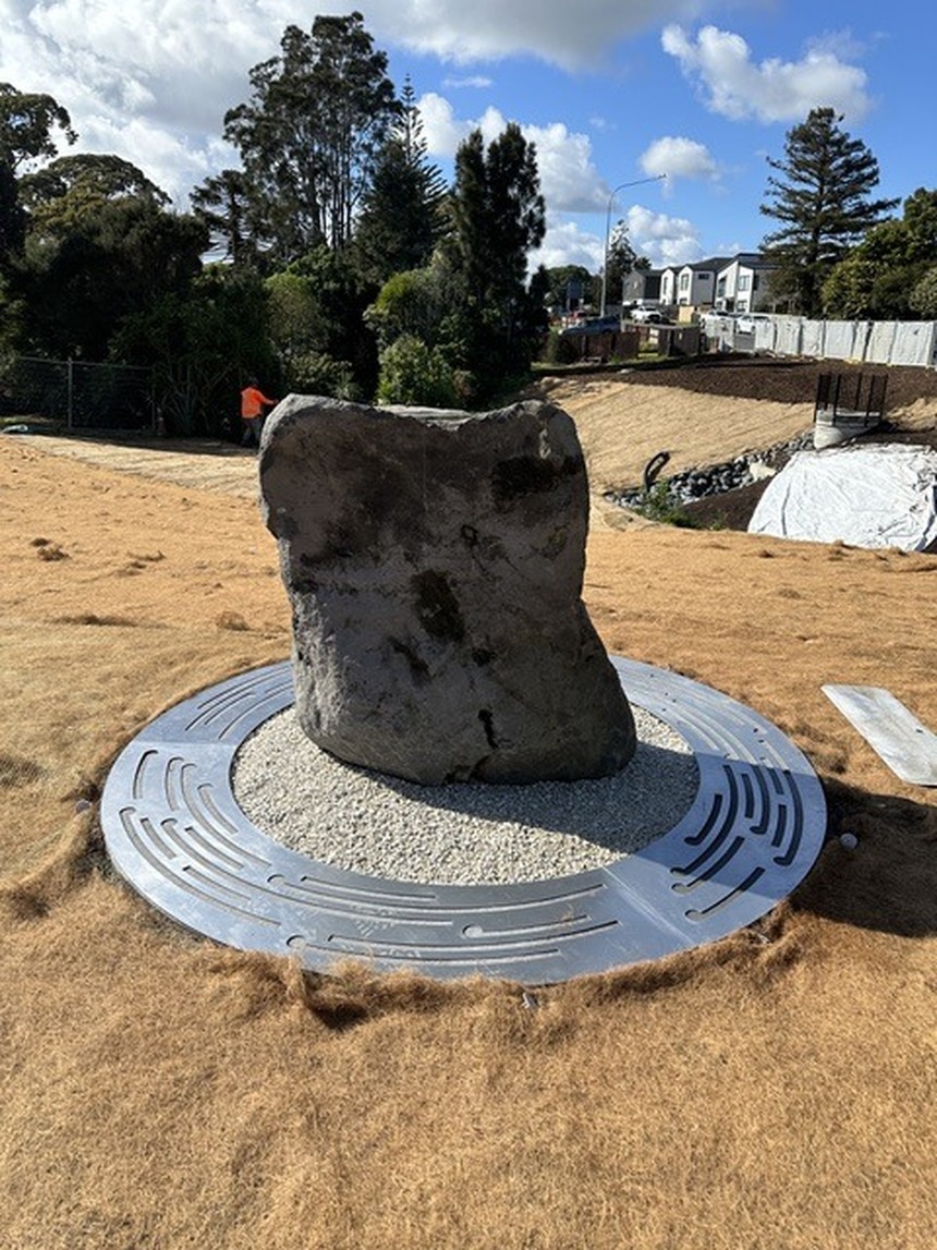 A weathered standing stone on a circular perforated-metal disc set into a gravel bed